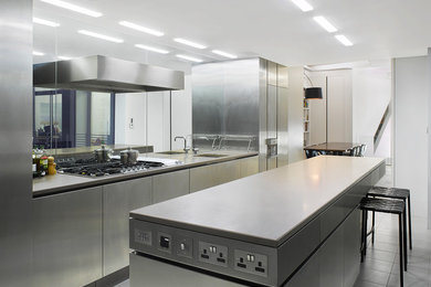 Large contemporary galley open plan kitchen in London with a built-in sink, stainless steel cabinets, metallic splashback, mirror splashback, stainless steel appliances and an island.