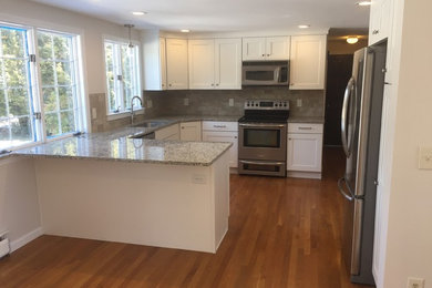 Example of a mid-sized classic u-shaped light wood floor eat-in kitchen design in New York with an undermount sink, shaker cabinets, white cabinets, granite countertops, beige backsplash, porcelain backsplash, stainless steel appliances and an island