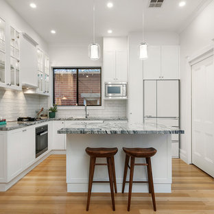Inspiration for a contemporary l-shaped kitchen in Melbourne with white splashback, multi-coloured benchtop, shaker cabinets, white cabinets, ceramic splashback, white appliances, light hardwood floors, with island and beige floor.
