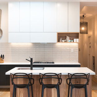 Small contemporary l-shaped open plan kitchen in Melbourne with a drop-in sink, flat-panel cabinets, white splashback, porcelain splashback, stainless steel appliances, light hardwood floors, beige floor and multiple islands.