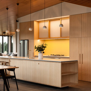 Photo of a mid-sized contemporary galley eat-in kitchen in Auckland with raised-panel cabinets, light wood cabinets, yellow splashback, glass sheet splashback, stainless steel appliances, porcelain floors and with island.