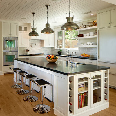Inspiration for a large timeless l-shaped light wood floor kitchen remodel in Santa Barbara with an undermount sink, shaker cabinets, white backsplash, paneled appliances, an island and black countertops