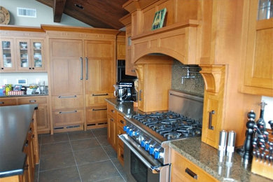 Ejemplo de cocina de estilo americano con puertas de armario de madera clara, encimera de granito, salpicadero verde, salpicadero de losas de piedra, electrodomésticos de acero inoxidable y una isla