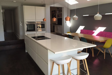 This is an example of a medium sized modern open plan kitchen in Manchester with flat-panel cabinets, white cabinets, quartz worktops, grey splashback, stainless steel appliances, dark hardwood flooring and an island.