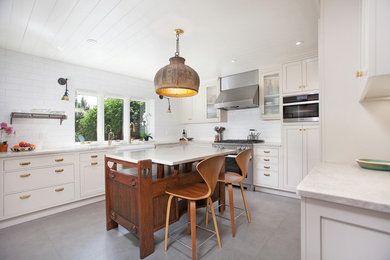 Example of a mid-sized arts and crafts u-shaped cement tile floor and gray floor enclosed kitchen design in San Diego with a farmhouse sink, shaker cabinets, white cabinets, marble countertops, white backsplash, subway tile backsplash, stainless steel appliances, an island and white countertops