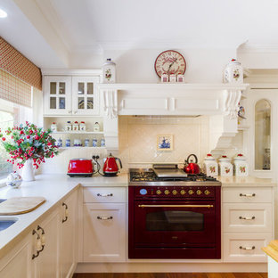 This is an example of a large country u-shaped separate kitchen in Melbourne with an undermount sink, shaker cabinets, white cabinets, wood benchtops, white splashback, ceramic splashback, coloured appliances, medium hardwood floors, with island, brown floor and beige benchtop.
