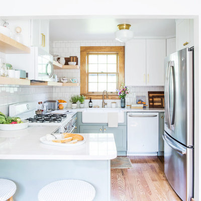 Example of a small transitional u-shaped medium tone wood floor and brown floor eat-in kitchen design in Other with a farmhouse sink, shaker cabinets, blue cabinets, quartz countertops, white backsplash, porcelain backsplash, white appliances and a peninsula