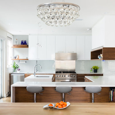Trendy u-shaped medium tone wood floor and brown floor eat-in kitchen photo in New York with an undermount sink, flat-panel cabinets, medium tone wood cabinets, glass tile backsplash, stainless steel appliances, an island and white countertops