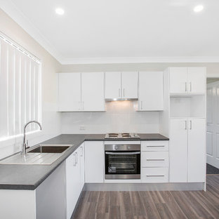 Inspiration for a mid-sized contemporary l-shaped open plan kitchen in Newcastle - Maitland with a single-bowl sink, louvered cabinets, white cabinets, laminate benchtops, white splashback, ceramic splashback, stainless steel appliances, vinyl floors, no island and brown floor.