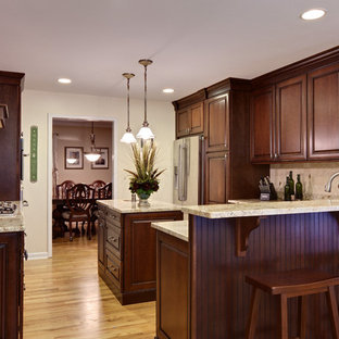 Inspiration pour une grand cuisine américaine traditionnelle en U avec un électroménager en acier inoxydable, un évier encastré, un placard avec porte à panneau surélevé, des portes de placard en bois sombre, un plan de travail en granite, une crédence beige, une crédence en carrelage de pierre, un sol en bois clair, un îlot central, un sol marron et un plan de travail beige.