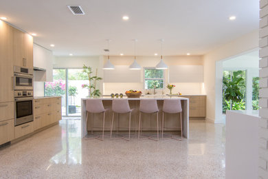 Large minimalist l-shaped terrazzo floor and multicolored floor open concept kitchen photo in Tampa with a farmhouse sink, flat-panel cabinets, light wood cabinets, solid surface countertops, white backsplash, stainless steel appliances, an island and white countertops