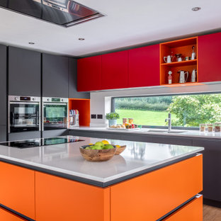 Photo of a midcentury l-shaped kitchen in Gloucestershire with a submerged sink, flat-panel cabinets, grey cabinets, window splashback, stainless steel appliances, medium hardwood flooring, an island, brown floors and white worktops.