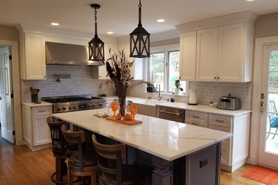 Inspiration for a large transitional l-shaped medium tone wood floor and brown floor eat-in kitchen remodel in New York with a farmhouse sink, recessed-panel cabinets, white cabinets, quartz countertops, white backsplash, ceramic backsplash, stainless steel appliances, an island and white countertops