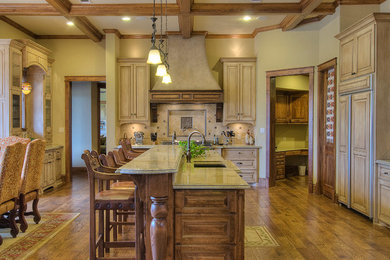 Mid-sized elegant l-shaped medium tone wood floor enclosed kitchen photo in Austin with raised-panel cabinets, light wood cabinets, granite countertops, beige backsplash, stone tile backsplash, stainless steel appliances, an island and a double-bowl sink