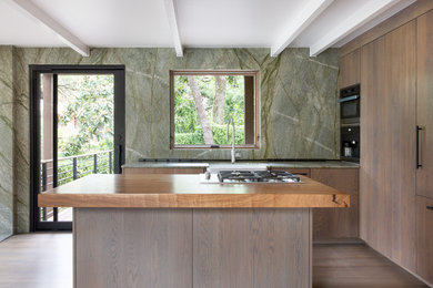 Example of a small minimalist l-shaped light wood floor and gray floor eat-in kitchen design in Austin with a farmhouse sink, flat-panel cabinets, medium tone wood cabinets, granite countertops, green backsplash, stone slab backsplash, stainless steel appliances, an island and green countertops