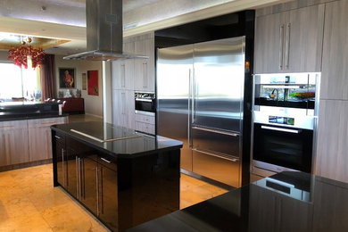 Example of a large trendy u-shaped ceramic tile and beige floor kitchen pantry design in Miami with a farmhouse sink, flat-panel cabinets, gray cabinets, granite countertops, black backsplash, an island and black countertops