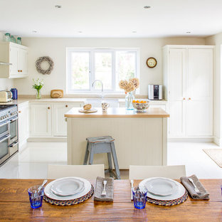 Large coastal l-shaped kitchen/diner in Buckinghamshire with a belfast sink, white cabinets, grey splashback, ceramic splashback, ceramic flooring, an island, white floors, shaker cabinets, wood worktops and stainless steel appliances.