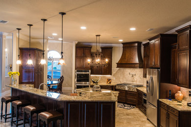 Large transitional l-shaped travertine floor and beige floor enclosed kitchen photo in Orlando with an undermount sink, raised-panel cabinets, dark wood cabinets, granite countertops, beige backsplash, mosaic tile backsplash, stainless steel appliances and an island