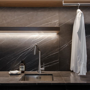 Photo of a large contemporary galley kitchen pantry in Sydney with a double-bowl sink, flat-panel cabinets, white cabinets, recycled glass benchtops, grey splashback, marble splashback, black appliances, porcelain floors, with island, grey floor and black benchtop.
