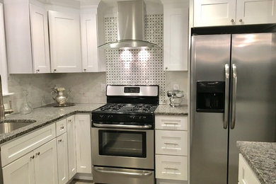 Mid-sized transitional u-shaped laminate floor and gray floor enclosed kitchen photo in Boston with an undermount sink, recessed-panel cabinets, white cabinets, granite countertops, white backsplash, stone tile backsplash, stainless steel appliances and an island