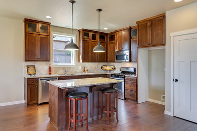 Mid-sized transitional l-shaped medium tone wood floor open concept kitchen photo in Portland with an undermount sink, shaker cabinets, medium tone wood cabinets, granite countertops, beige backsplash, ceramic backsplash, stainless steel appliances and an island