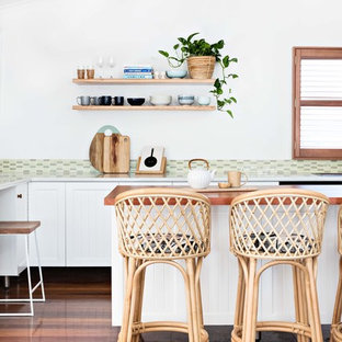 Inspiration for a beach style l-shaped kitchen in Wollongong with shaker cabinets, white cabinets, wood benchtops, green splashback, mosaic tile splashback, medium hardwood floors, with island, brown floor and brown benchtop.
