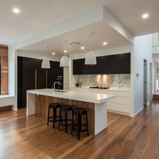 Photo of a contemporary galley kitchen in Brisbane with black cabinets, grey splashback, marble splashback, medium hardwood floors, with island, white benchtop, a double-bowl sink, flat-panel cabinets, black appliances and brown floor.