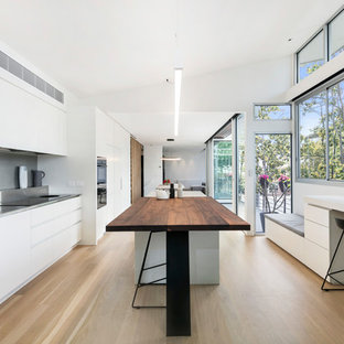 Design ideas for a modern galley open plan kitchen in Melbourne with an integrated sink, flat-panel cabinets, white cabinets, stainless steel benchtops, grey splashback, panelled appliances, light hardwood floors, with island and beige floor.