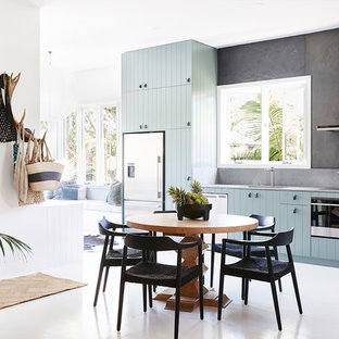 Design ideas for a mid-sized tropical l-shaped eat-in kitchen in Sydney with an undermount sink, flat-panel cabinets, quartz benchtops, grey splashback, slate splashback, stainless steel appliances, painted wood floors, white floor, grey benchtop and blue cabinets.