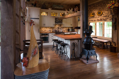Example of a cottage single-wall dark wood floor eat-in kitchen design in New York with a farmhouse sink, recessed-panel cabinets, white cabinets, paneled appliances, wood countertops, gray backsplash and stone tile backsplash