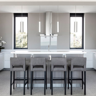 Contemporary u-shaped kitchen in Sussex with flat-panel cabinets, white cabinets, grey splashback, glass sheet splashback, black appliances, an island, grey floors and white worktops.