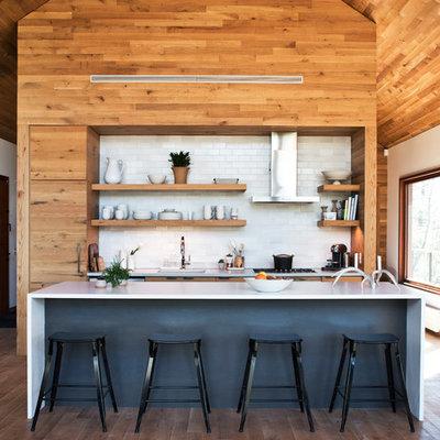 Mid-sized trendy galley medium tone wood floor and brown floor kitchen photo in New York with an undermount sink, flat-panel cabinets, medium tone wood cabinets, white backsplash, subway tile backsplash, paneled appliances, an island, white countertops and solid surface countertops