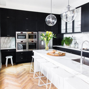 Foto de cocina clásica renovada con puertas de armario negras, encimera de mármol, salpicadero blanco, electrodomésticos de acero inoxidable, suelo de madera en tonos medios, fregadero bajoencimera y suelo beige