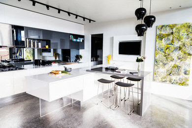 Cette image montre une cuisine américaine linéaire design avec des portes de placard blanches, une crédence miroir, sol en béton ciré et îlot.