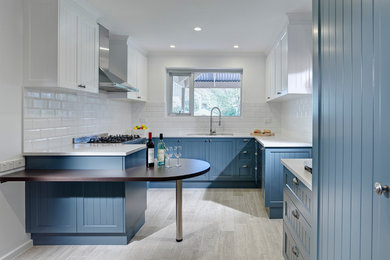 他の地域にある高級な小さなトラディショナルスタイルのおしゃれなキッチン (アンダーカウンターシンク、落し込みパネル扉のキャビネット、青いキャビネット、白いキッチンパネル、サブウェイタイルのキッチンパネル、シルバーの調理設備、ベージュの床) の写真