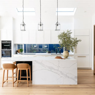 Inspiration för stora maritima vitt parallellkök, med skåp i shakerstil, vita skåp, marmorbänkskiva, en köksö, fönster som stänkskydd, integrerade vitvaror, mellanmörkt trägolv och brunt golv
