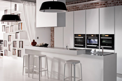 Photo of a medium sized modern galley kitchen/diner in London with a submerged sink, flat-panel cabinets, white cabinets, composite countertops, black appliances and an island.