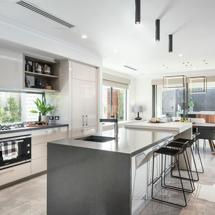 This is an example of a contemporary galley eat-in kitchen in Perth with an undermount sink, flat-panel cabinets, beige cabinets, window splashback, black appliances, with island and beige floor.