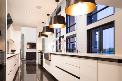 Design ideas for a large contemporary galley kitchen in Edmonton with a belfast sink, flat-panel cabinets, white cabinets, engineered stone countertops, black splashback, porcelain splashback, black appliances, porcelain flooring and an island.