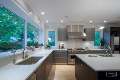 Exempel på ett stort modernt kök, med en integrerad diskho, släta luckor, grå skåp, vitt stänkskydd, stänkskydd i tunnelbanekakel, rostfria vitvaror, ljust trägolv och en köksö