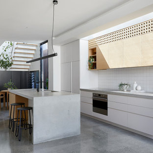 Inspiration for a mid-sized contemporary galley open plan kitchen in Melbourne with light wood cabinets, concrete benchtops, white splashback, ceramic splashback, stainless steel appliances, concrete floors, with island, grey floor, grey benchtop, an integrated sink and flat-panel cabinets.