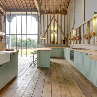 This is an example of an expansive country galley open plan kitchen in Other with a farmhouse sink, green cabinets, light hardwood floors and with island.