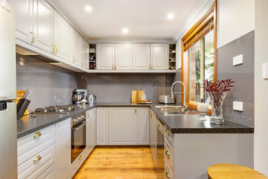 Contemporary u-shaped kitchen in Sydney with a built-in sink, raised-panel cabinets, grey cabinets, grey splashback, stainless steel appliances, medium hardwood flooring, a breakfast bar, brown floors and black worktops.