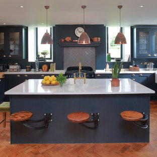 Foto de cocina en U, clásica, de tamaño medio, con fregadero sobremueble, encimera de acrílico, suelo de madera en tonos medios, una isla, puertas de armario azules, salpicadero de azulejos de cerámica, armarios tipo vitrina, salpicadero verde, electrodomésticos negros y suelo naranja