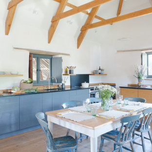 Large rural l-shaped open plan kitchen in Cornwall with flat-panel cabinets, granite worktops, black splashback, stainless steel appliances, medium hardwood flooring, brown floors, black worktops, a submerged sink, blue cabinets and no island.