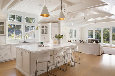 Foto på ett maritimt kök med öppen planlösning, med en enkel diskho, luckor med infälld panel, vita skåp, marmorbänkskiva, vitt stänkskydd, stänkskydd i stenkakel, rostfria vitvaror, ljust trägolv och en köksö