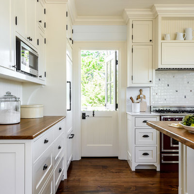 Cottage l-shaped medium tone wood floor and brown floor kitchen photo in Seattle with shaker cabinets, white cabinets, wood countertops, white backsplash, an island and brown countertops