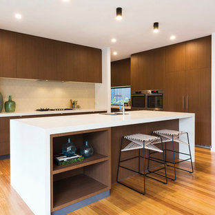 Photo of a contemporary kitchen in Melbourne with a single-bowl sink, flat-panel cabinets, dark wood cabinets, beige splashback, medium hardwood floors, with island, white benchtop and panelled appliances.
