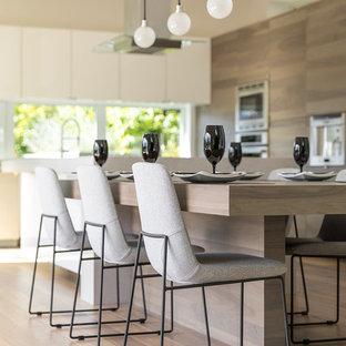 Geräumige Moderne Wohnküche in L-Form mit Unterbauwaschbecken, flächenbündigen Schrankfronten, grauen Schränken, Quarzit-Arbeitsplatte, Rückwand-Fenster, Küchengeräten aus Edelstahl, braunem Holzboden, zwei Kücheninseln und braunem Boden in Vancouver