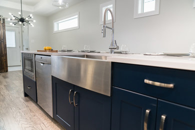 Eat-in kitchen - modern galley dark wood floor and brown floor eat-in kitchen idea in Other with a farmhouse sink, shaker cabinets, blue cabinets, white backsplash, subway tile backsplash, stainless steel appliances, an island and white countertops